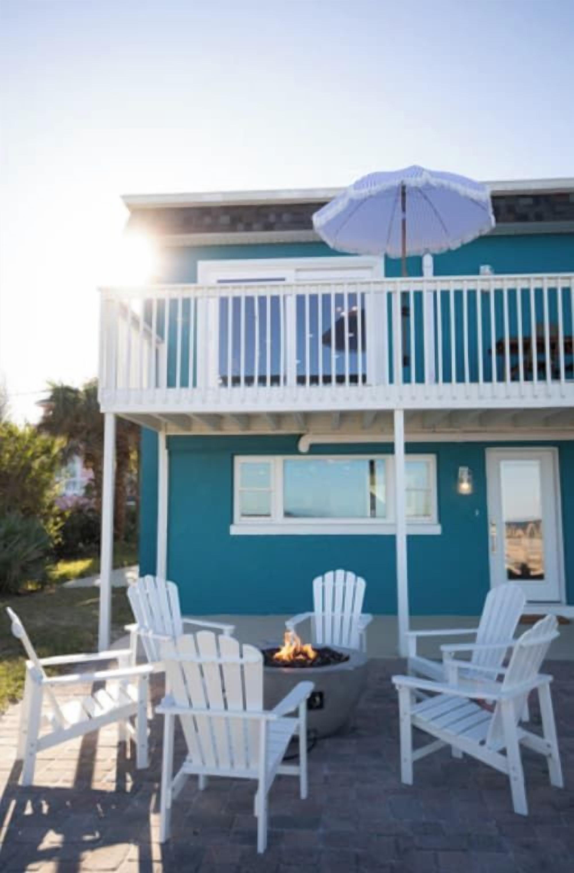 A two-story building with a balcony, outdoor seating with white chairs, and a fire pit.