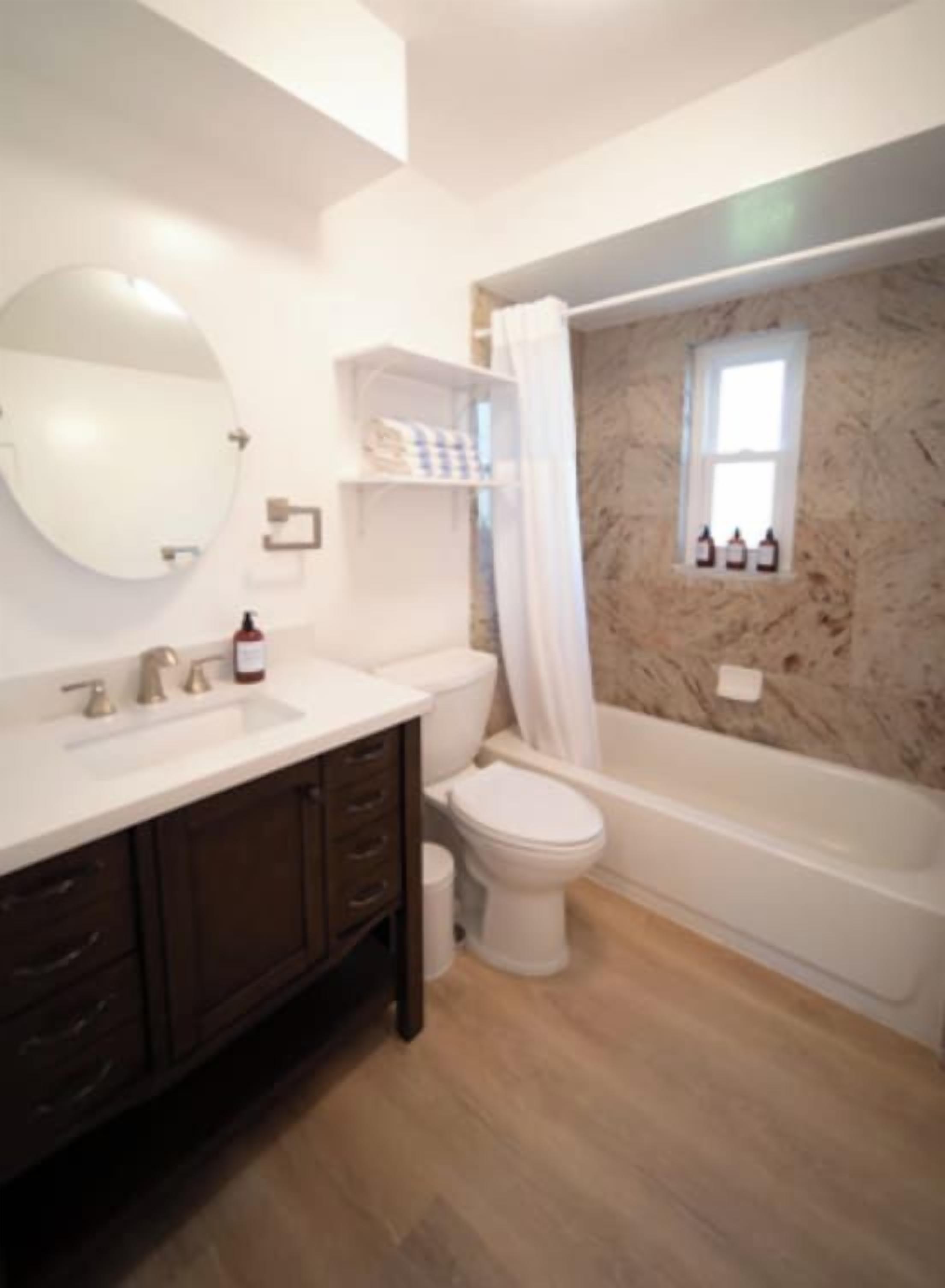 A bathroom with a marble wall, a bathtub, a toilet, and a sink.