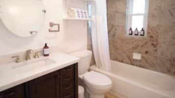 A bathroom with a marble wall, a bathtub, a toilet, and a sink.