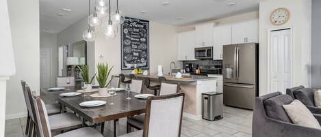 A modern kitchen with a central island, stainless steel appliances, and a dining area with a dark wooden table and chairs.