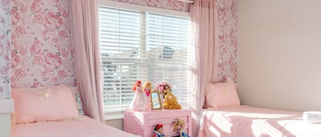 A bedroom with two beds, a vanity with dolls, and floral wallpaper.