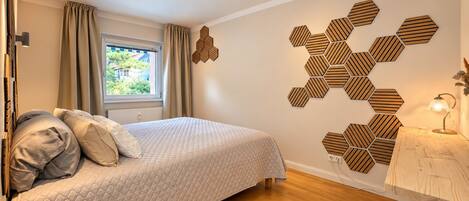 Un dormitorio moderno con cama, suelo de madera, una ventana con cortinas y un patrón hexagonal en la pared.