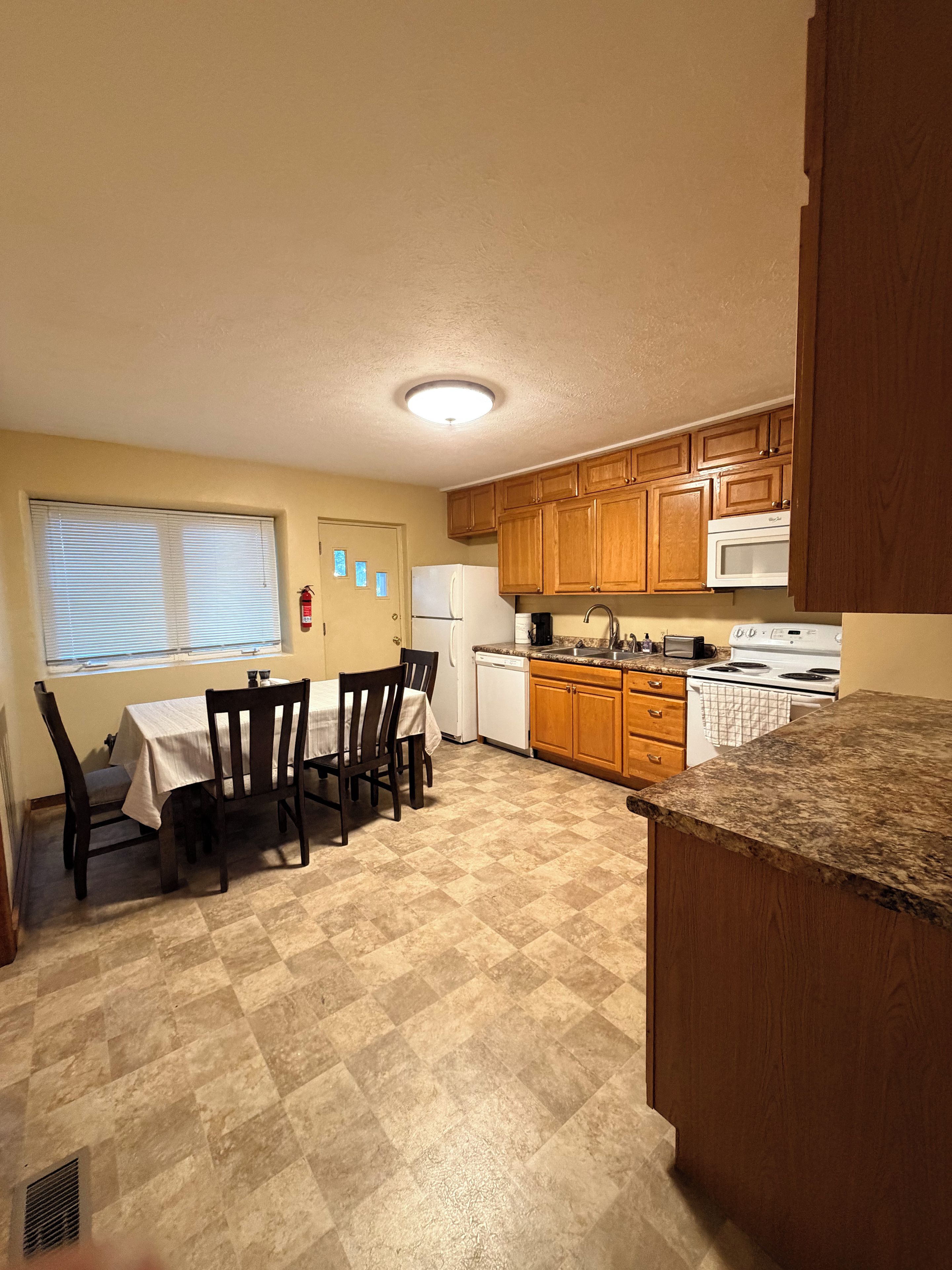 A kitchen with wooden cabinets, a microwave, a dishwasher, and a dining area with a table and chairs.