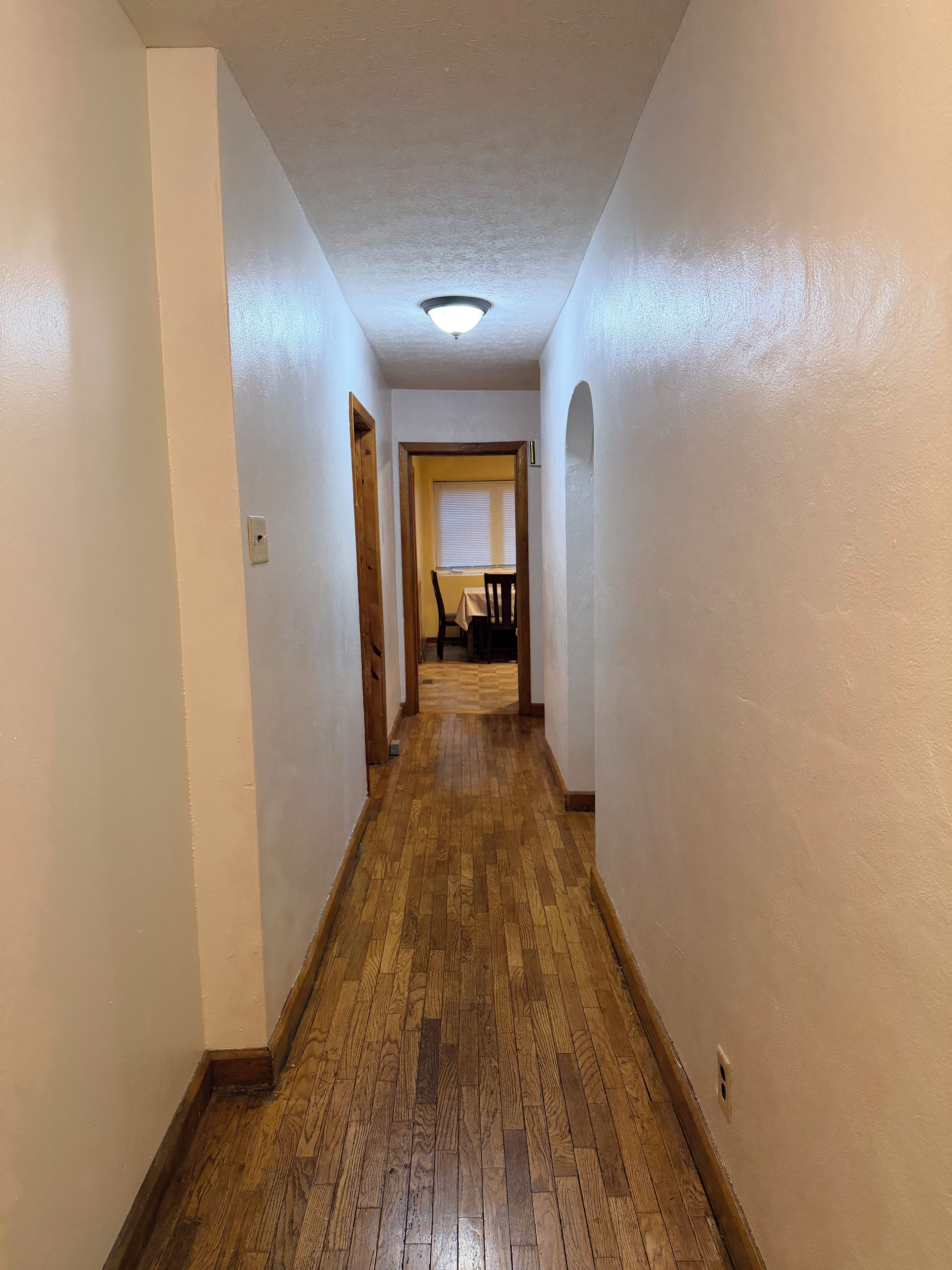 A hallway with wooden flooring, white walls, and a ceiling light.