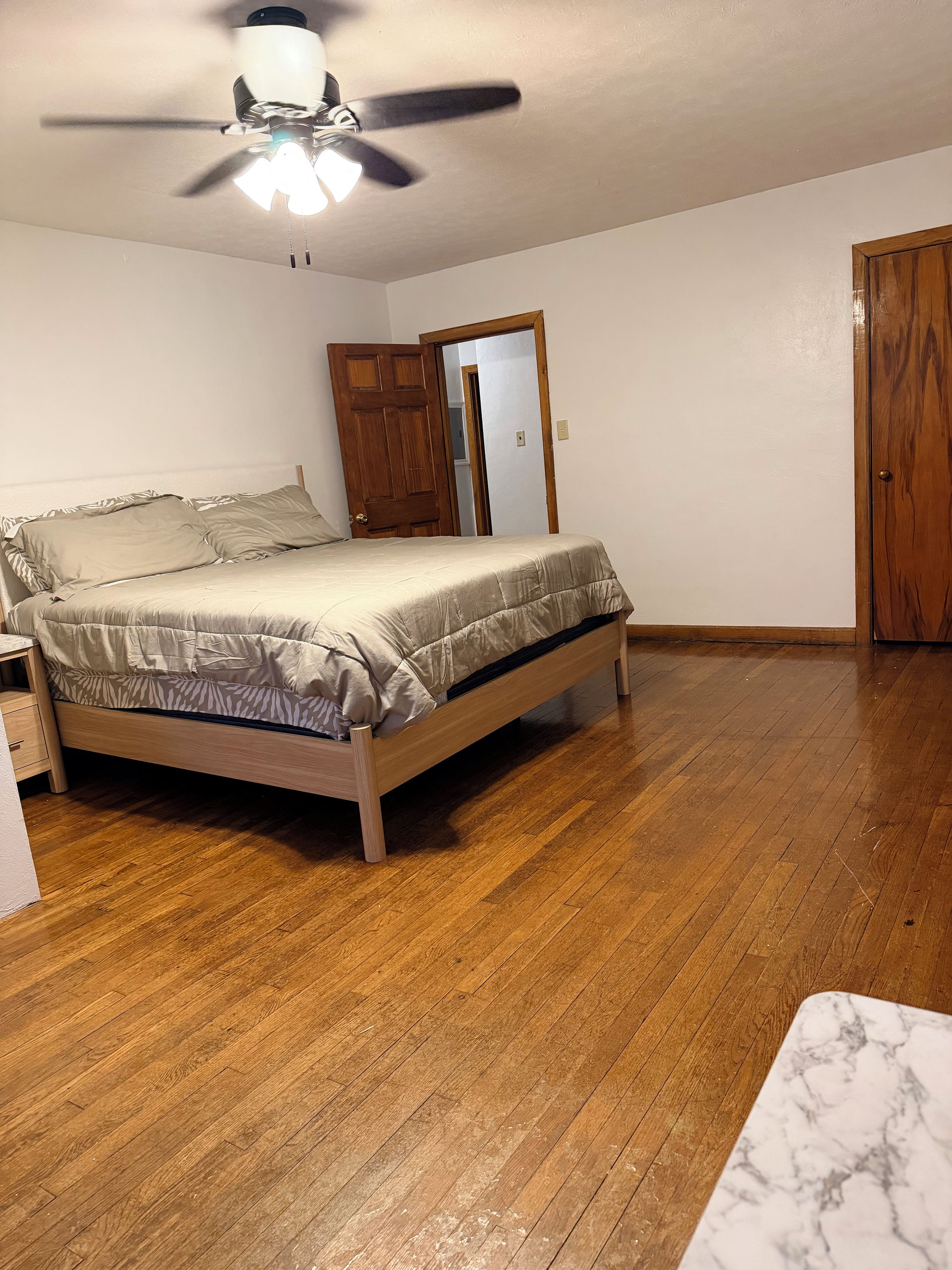 A bedroom with a wooden bed, a ceiling fan, and a wooden door.