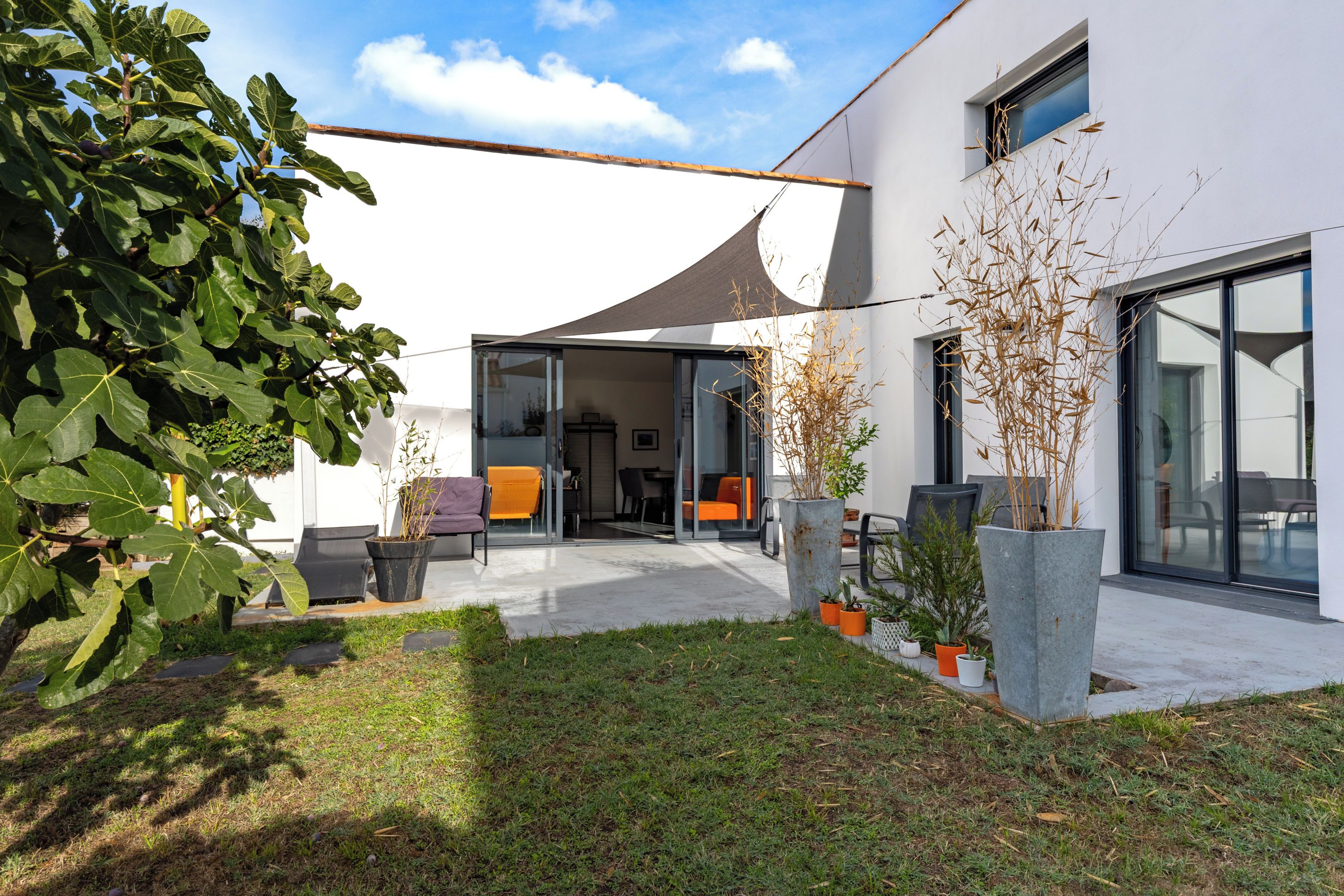 Una casa moderna con un patio, mobiliario exterior y un ventanal amplio.