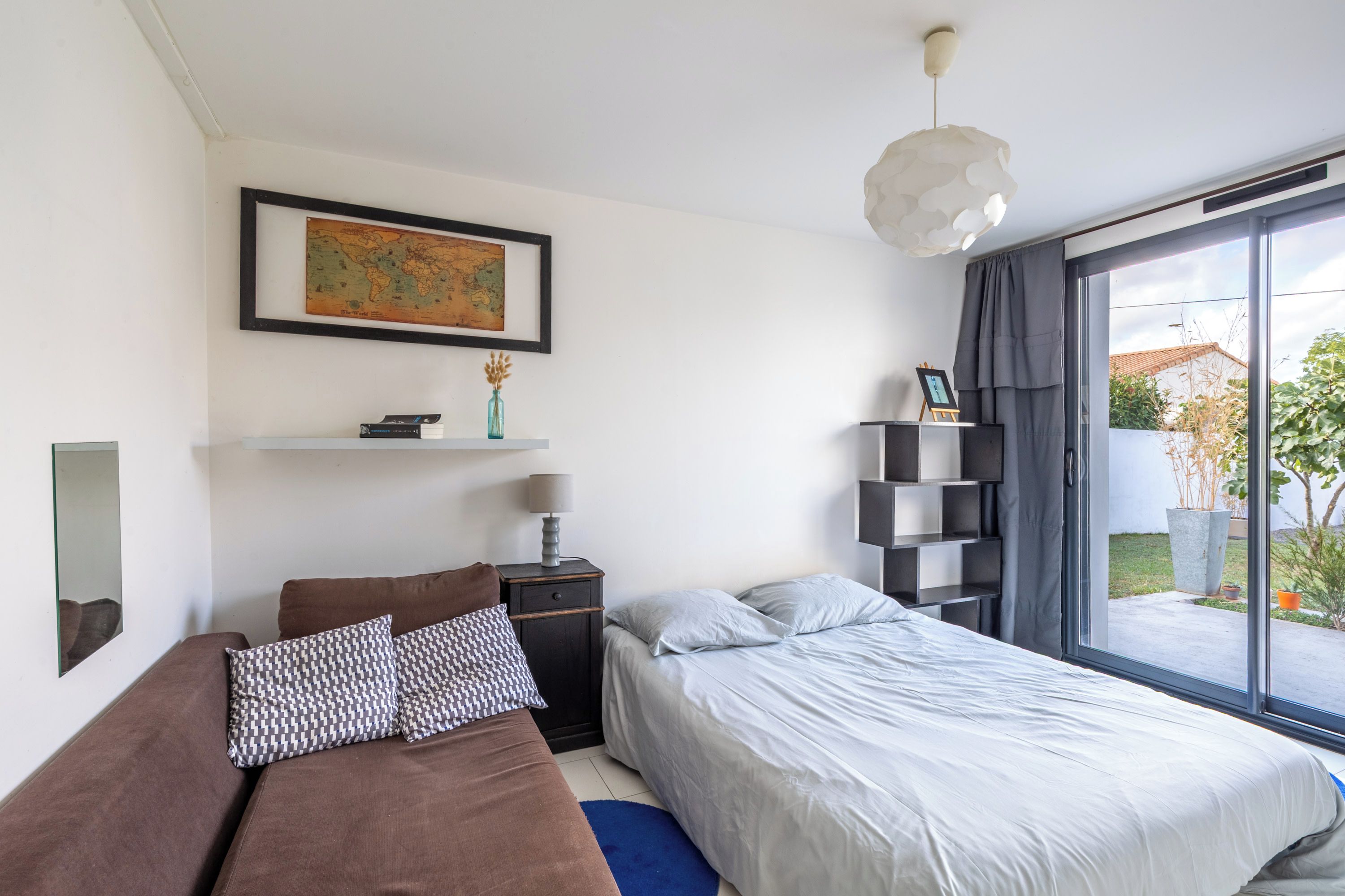 Un dormitorio moderno con cama, mesita de noche, lámpara, un mapa en la pared y vistas al exterior.