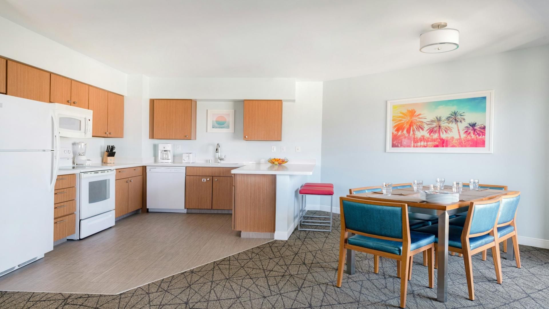 A modern kitchen with white appliances, wooden cabinets, and a dining area with blue chairs and a table.
