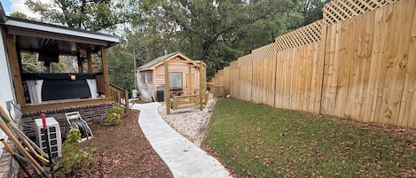 Een houten chalet met een veranda en een klein tuinhuisje, omgeven door een houten hek en een betonnen pad.