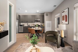 A modern kitchen with grey cabinets, a microwave, and a dining area with a table and chairs. - Duck Island 1BR , Walk to Ohio City + Parking (Cleveland)