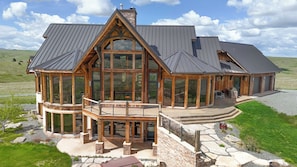 A large, modern house with a prominent central glass structure, a stone foundation, and a metal roof.