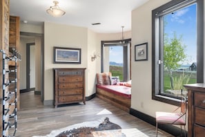 A room with a wooden bench, a dresser, and a large window with a view of the outdoors.