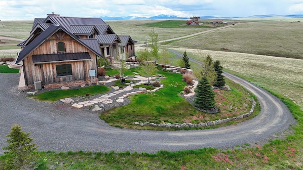 A rustic wooden house with a stone pathway leading to the entrance, surrounded by a well-maintained lawn and a few trees.