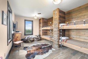 A room with bunk beds, a desk, a chair, and a large rug.