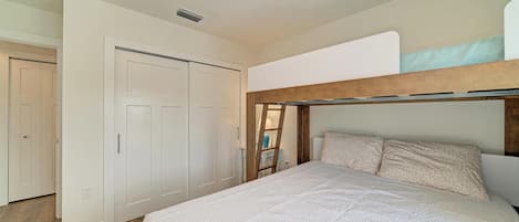A bedroom with a bunk bed, white walls, a wooden headboard, and a ceiling light fixture.