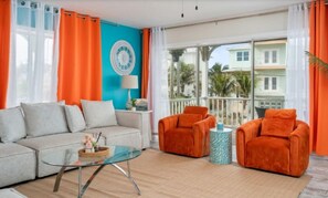 Ein Wohnzimmer mit einer Couch, zwei Sesseln, einem Couchtisch und Blick auf ein Gebäude durch große Fenster.
