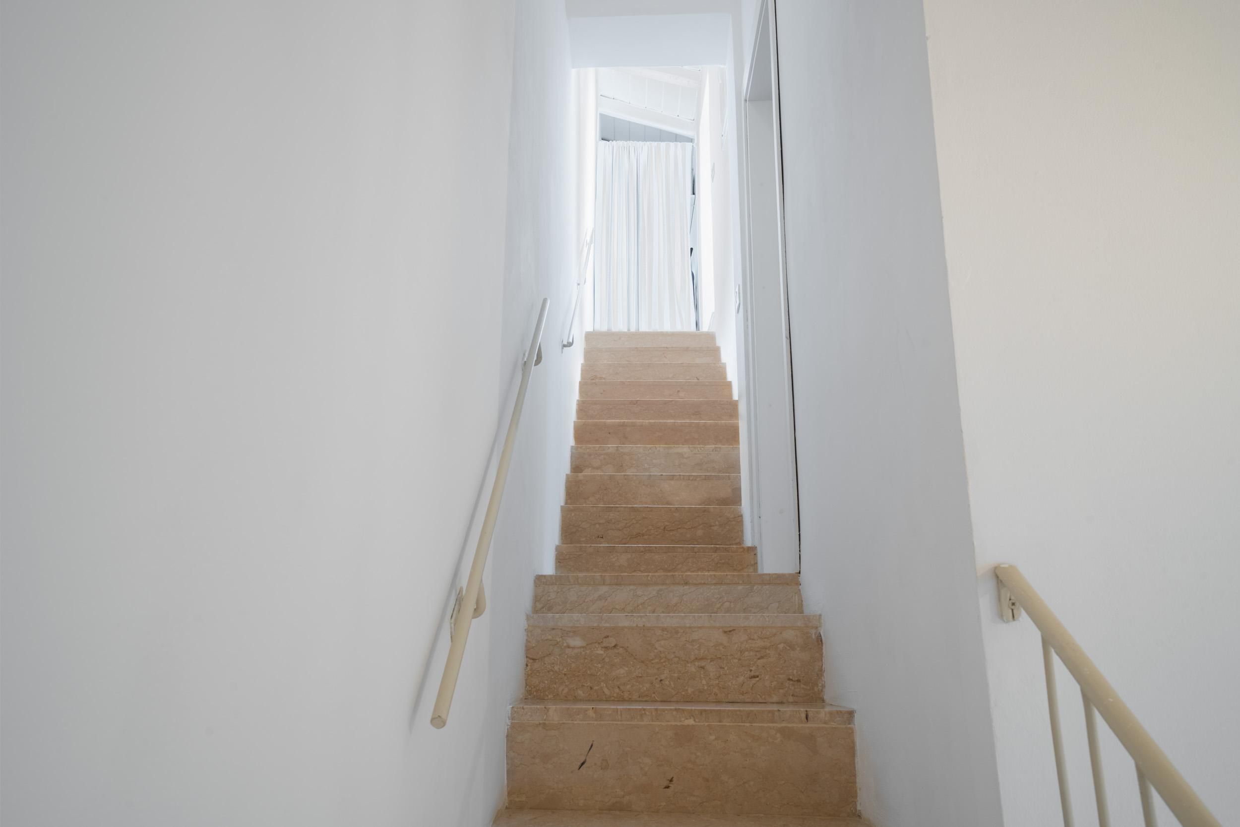 A staircase with beige steps leading upwards, white walls, and a handrail on the right.