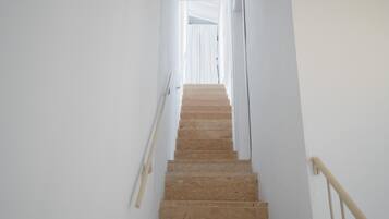 A staircase with beige steps leading upwards, white walls, and a handrail on the right.