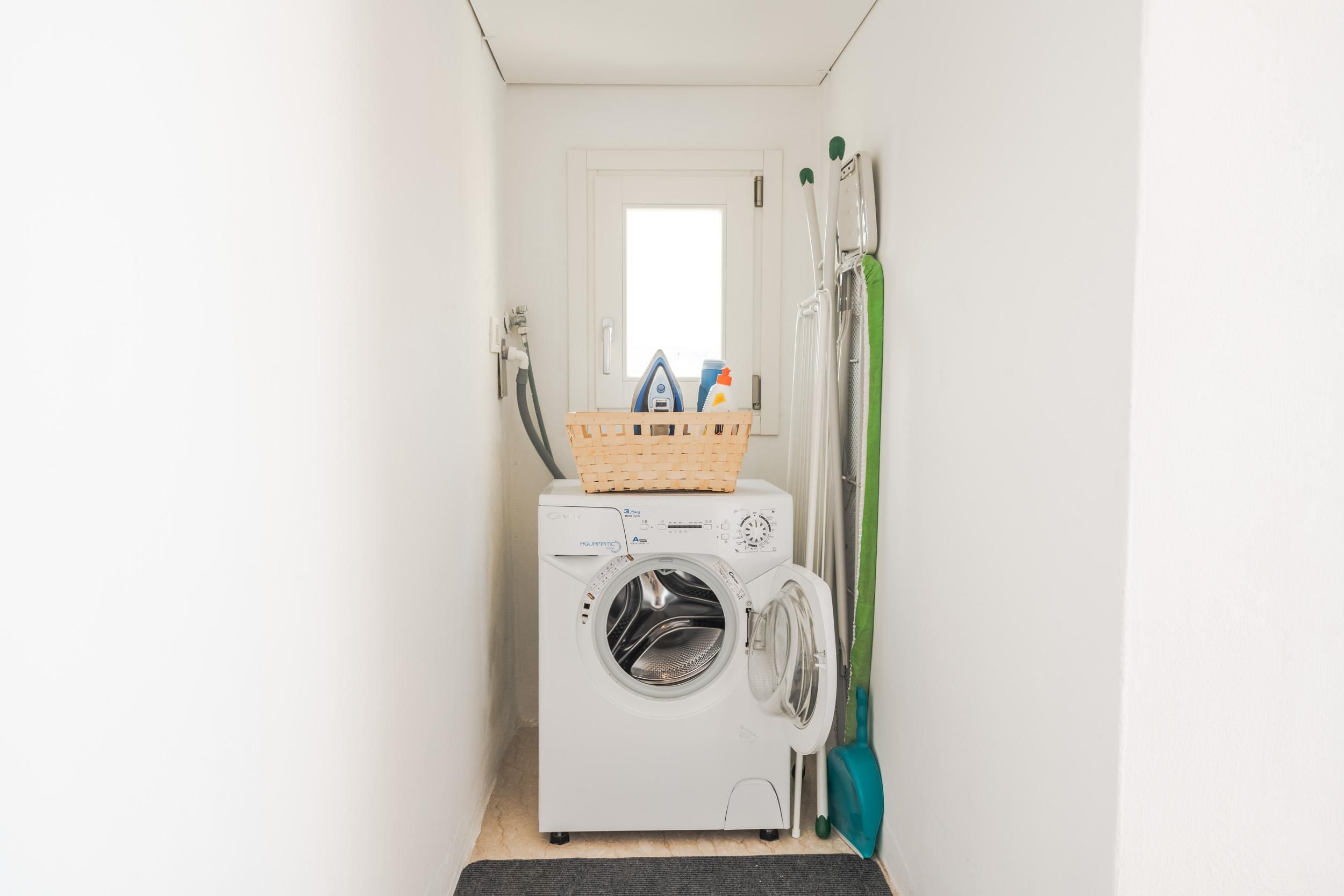 A compact laundry room with a front-loading washing machine, a drying rack, and a basket on top.
