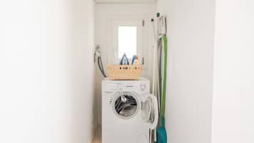 A compact laundry room with a front-loading washing machine, a drying rack, and a basket on top.