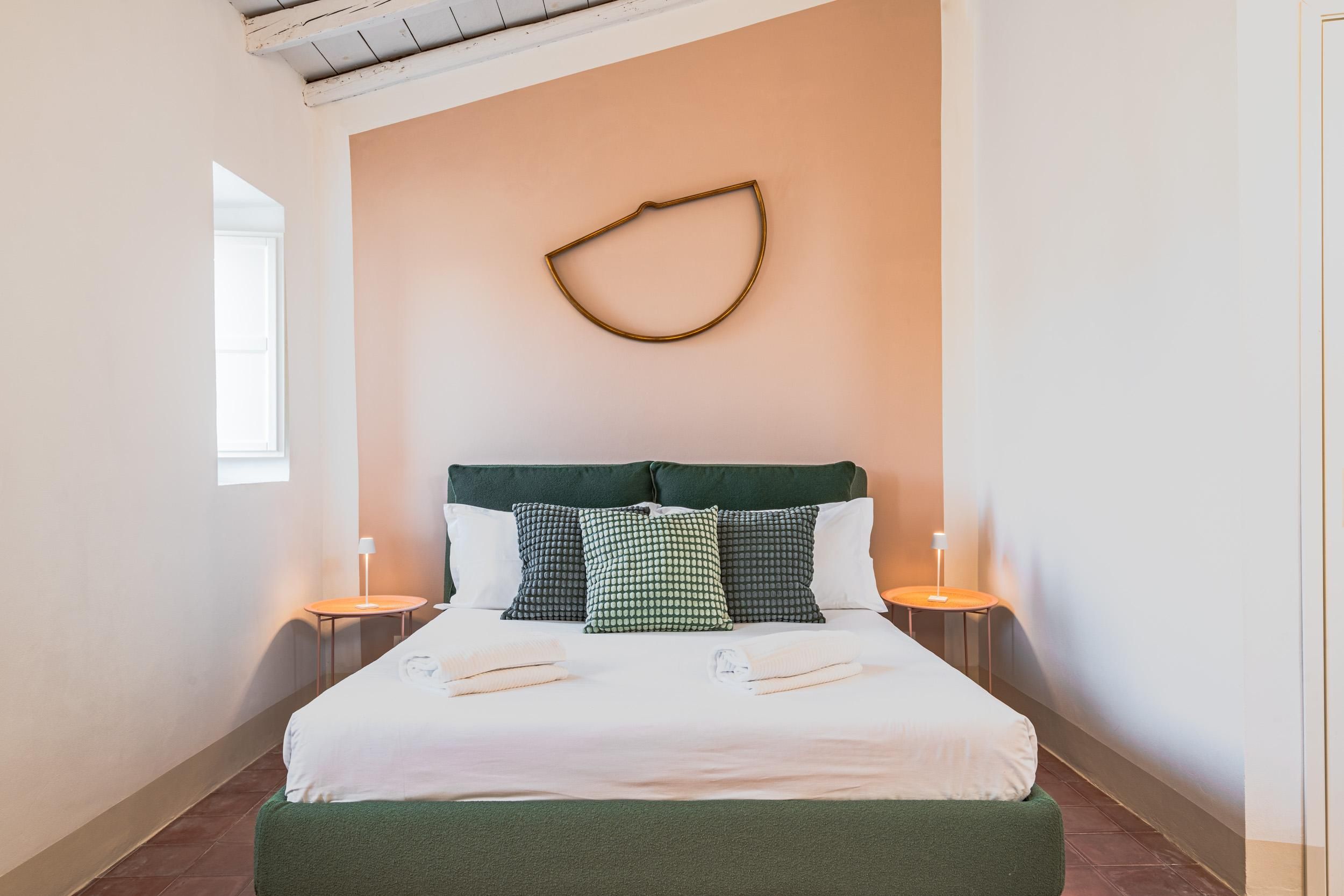 A hotel room with a bed, pillows, bedside lamps, and a wall-mounted light fixture.
