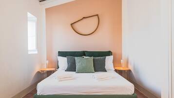 A hotel room with a bed, pillows, bedside lamps, and a wall-mounted light fixture.