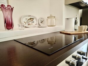A kitchen with a modern induction cooktop, a glass vase, ceramic plates, a jar, and a water bottle. - Maestranza72   one bedroom luxury flat in Ortigia (SIRACUSA)