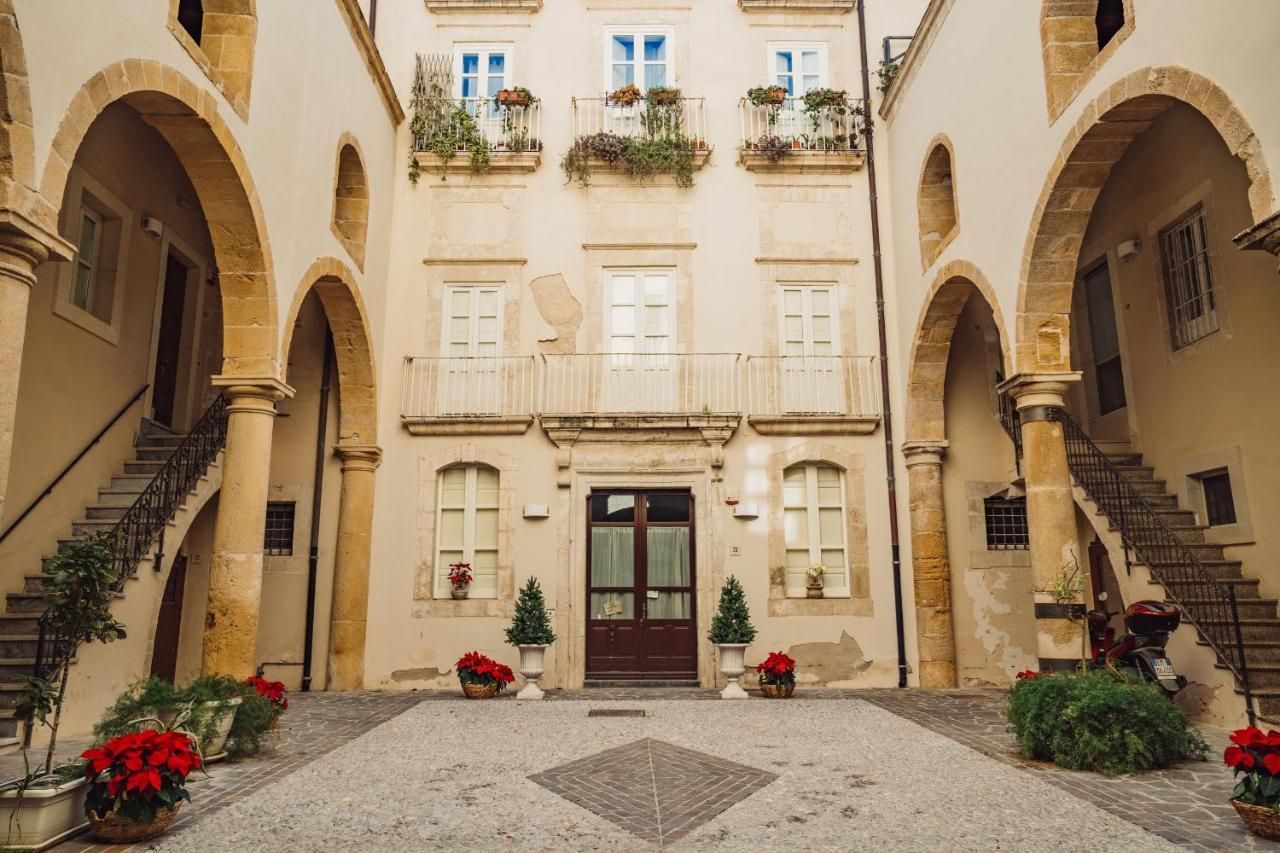 A courtyard with a central door, flanked by arches and balconies with potted plants.
