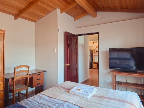 A bedroom with a bed, a desk, a chair, a television, and a door leading to another room. - Nice View | Terrace & Wood (Cusco)
