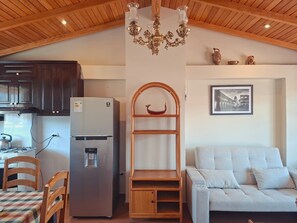 A compact kitchen with a refrigerator, a wooden shelf, and a dining area with a table and chairs. - Nice View | Terrace & Wood (Cusco)