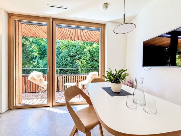 A modern dining area with a white table, two chairs, a potted plant, and a mounted TV. - Selva 42 by Interhome (Flims)