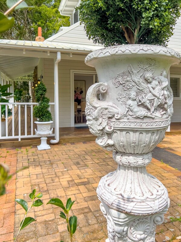 Una urna blanca ornamentada con un árbol y figuras, ubicada en un patio de ladrillo.