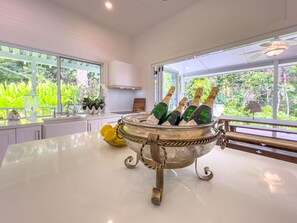 Una cocina con una isla grande, un enfriador de vinos con botellas y vistas al exterior con vegetación.