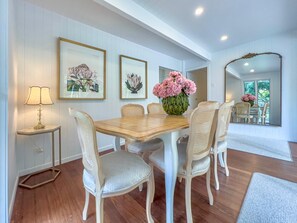 Un comedor con una mesa de madera, seis sillas, un florero y dos cuadros en la pared.