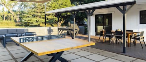 Une terrasse extérieure équipée d’une table de ping-pong, d’un espace salon et d’une partie abritée avec des tables et des chaises.