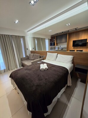 A modern hotel room with a large bed, a flat-screen TV, a sofa, and a dining area. - Luxury beachfront apartment with everything you need on the same block. (João Pessoa)