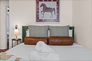 Hotelkamer met een bed, kussens, een aan de muur hangend schilderij van een paard, een bedlampje en een deur.