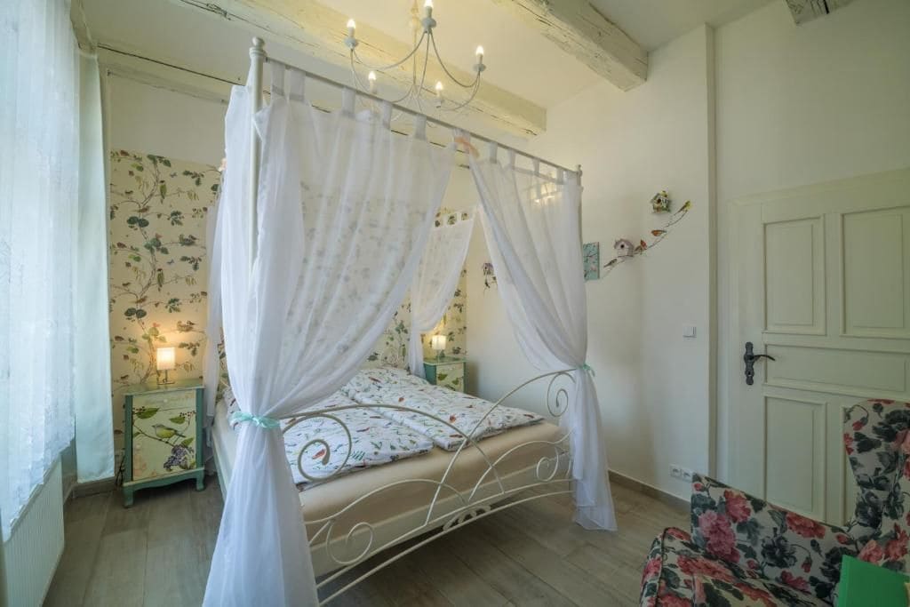 Une chambre avec un lit à baldaquin, un fauteuil à motifs floraux et une porte dotée d’une poignée.