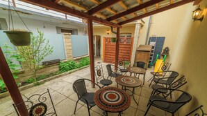 Un patio al aire libre con varias mesas y sillas, una maceta colgante y una puerta de madera.