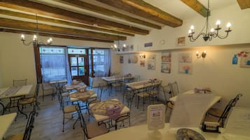 A restaurant interior with wooden beams, tables, chairs, and wall-mounted lights.