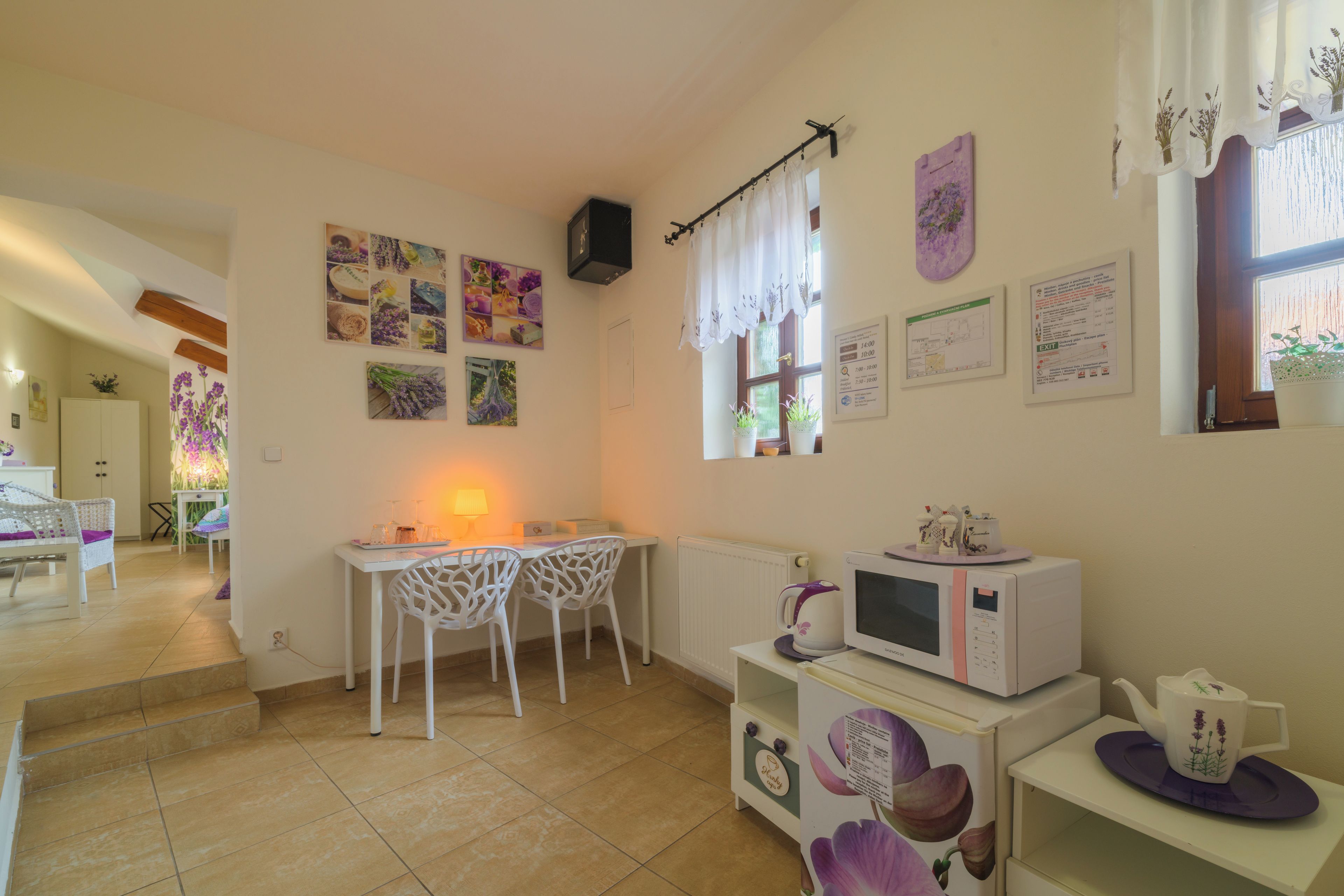 Cocina compacta con comedor, una mesa blanca, dos sillas, microondas y hervidor en una estantería.