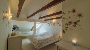 Un dormitorio con techo inclinado, vigas de madera, cama con ropa de cama floral, escritorio con ventilador y pared con adhesivos florales.