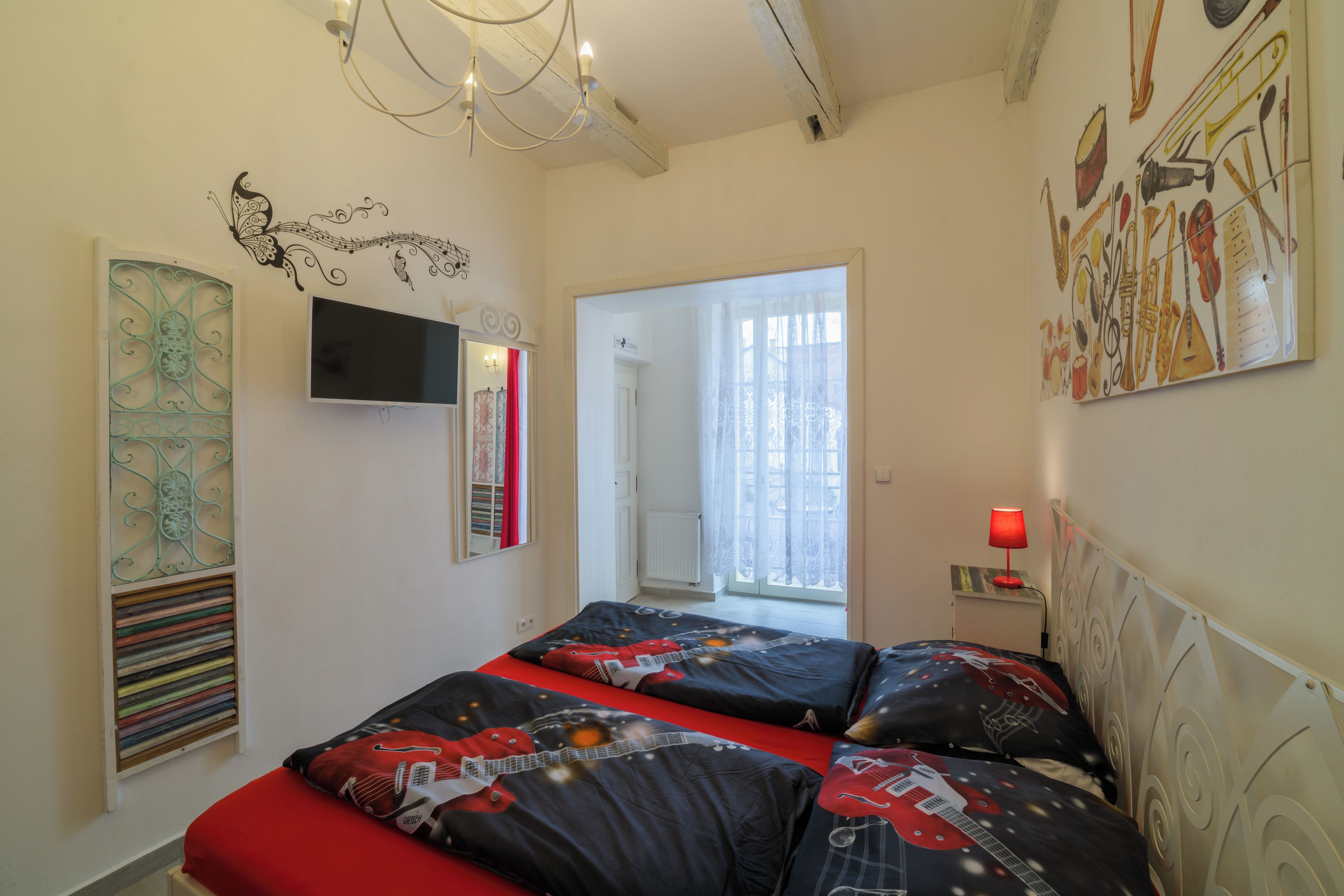 Un dormitorio con una cama, televisor, ventana con cortinas y una pared con instrumentos musicales.