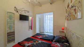 Un dormitorio con una cama, televisor, ventana con cortinas y una pared con instrumentos musicales.