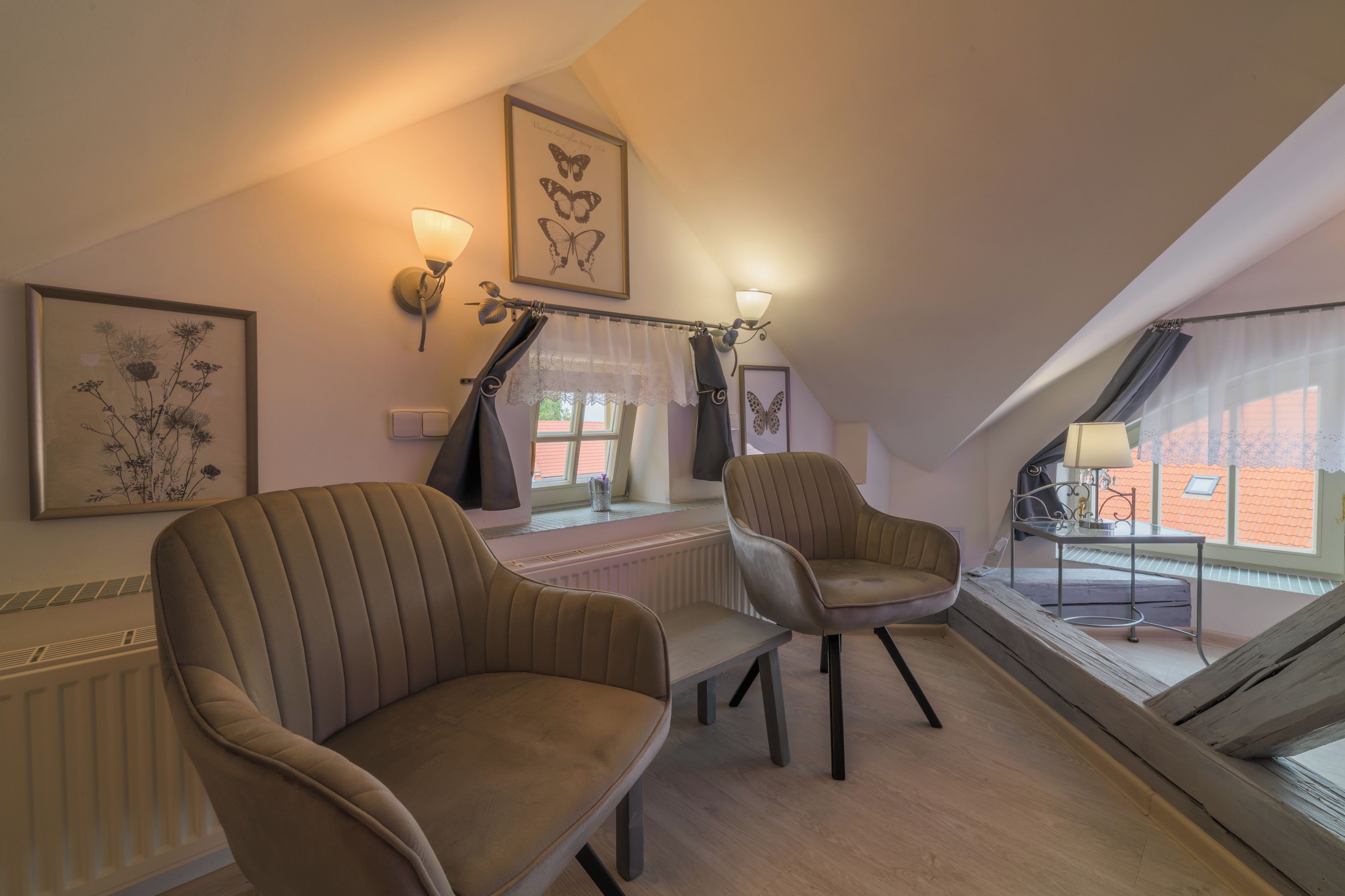 A cozy attic room with two upholstered chairs, a table, and a view of the outside through a window.