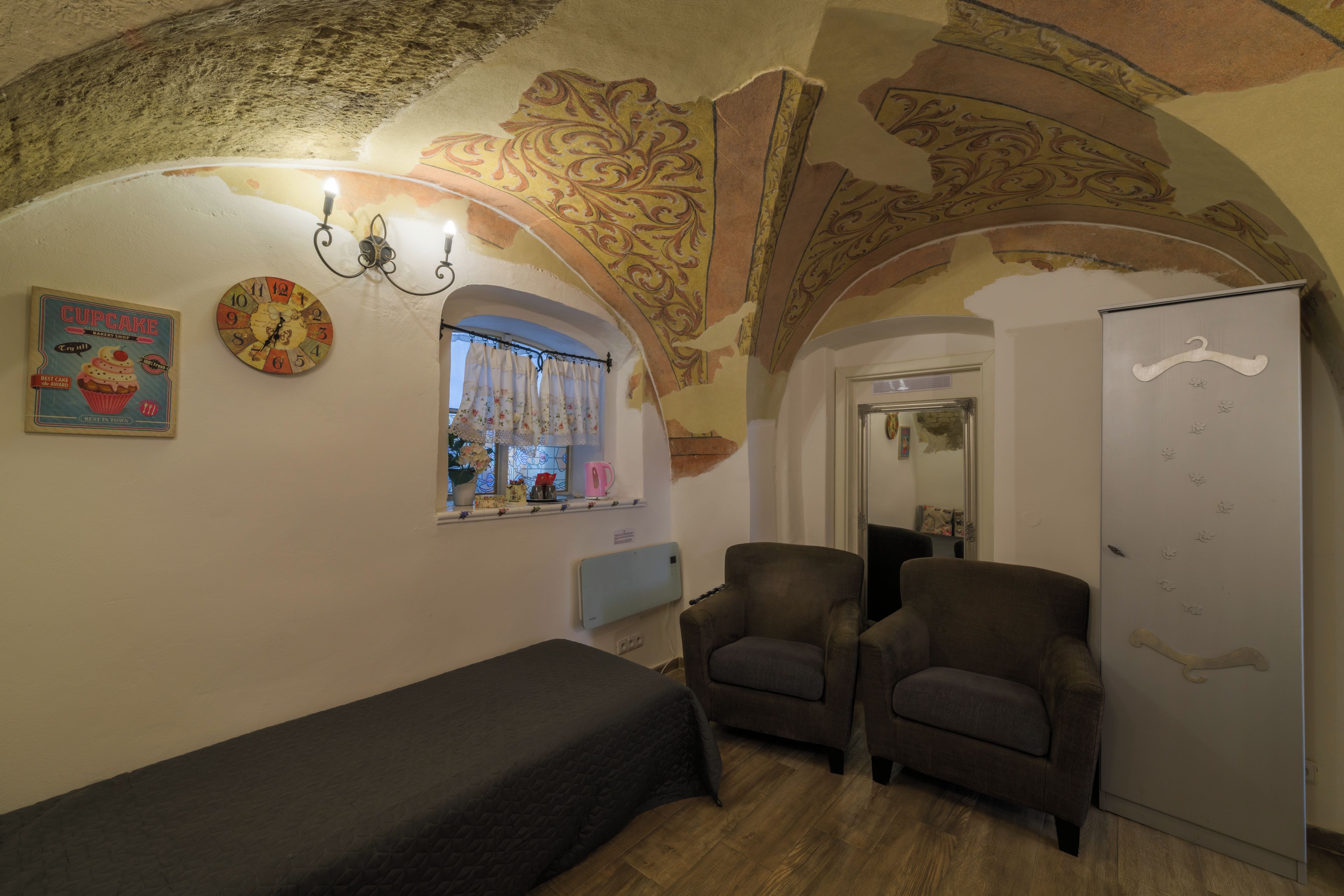 A room with a bed, two armchairs, a wall clock, and a decorative ceiling.