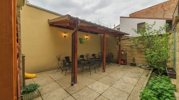 Un patio con una pérgola, mobiliario exterior y plantas en macetas.