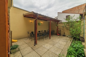 Un patio con una pérgola, mobiliario exterior y plantas en macetas.
