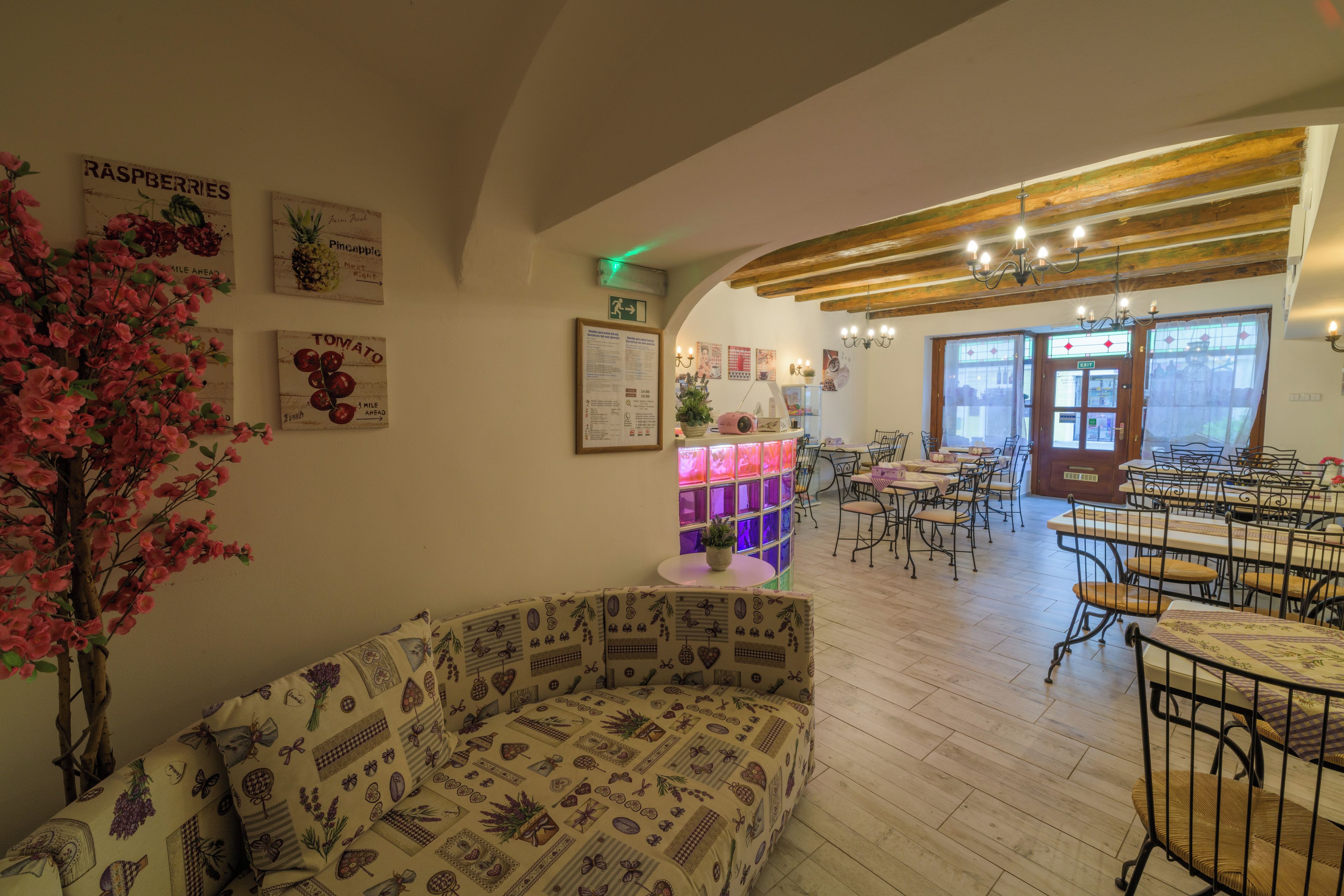 A cozy cafe interior with a wooden ceiling, a central table with chairs, and wall decorations including a sign for 'Raspberries' and 'Pineapple'.