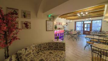 A cozy cafe interior with a wooden ceiling, a central table with chairs, and wall decorations including a sign for 'Raspberries' and 'Pineapple'.